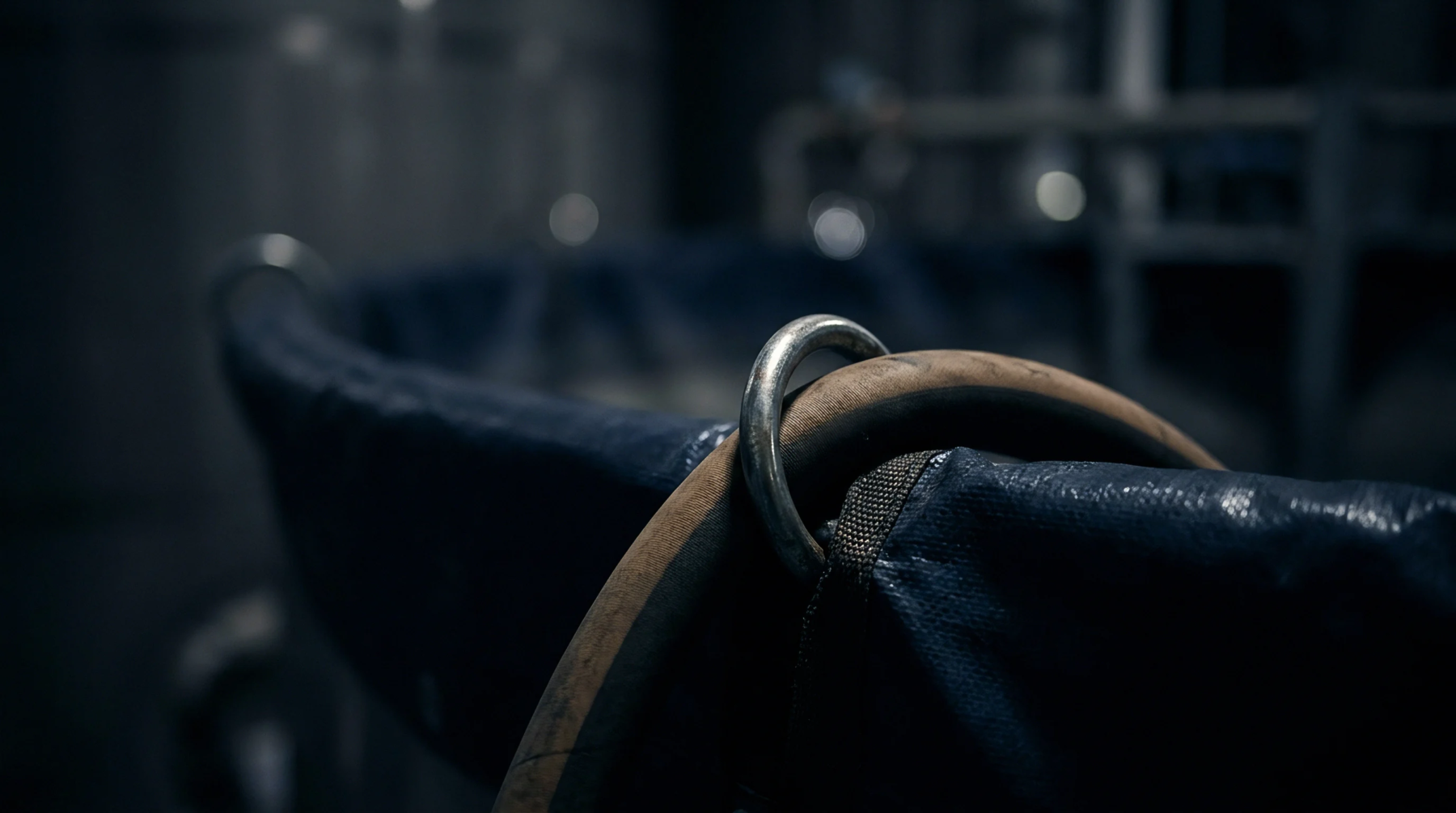 A reinforced polymer hopper liner with a metallic ring sits within a dark industrial manufacturing facility used for raw material containment.
