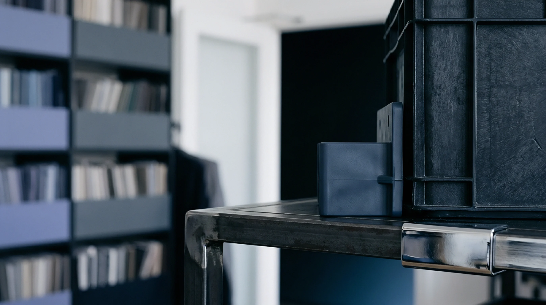 An injection moulded polymer component rests beside a heavy duty plastic crate on a metal workbench in a product design studio.