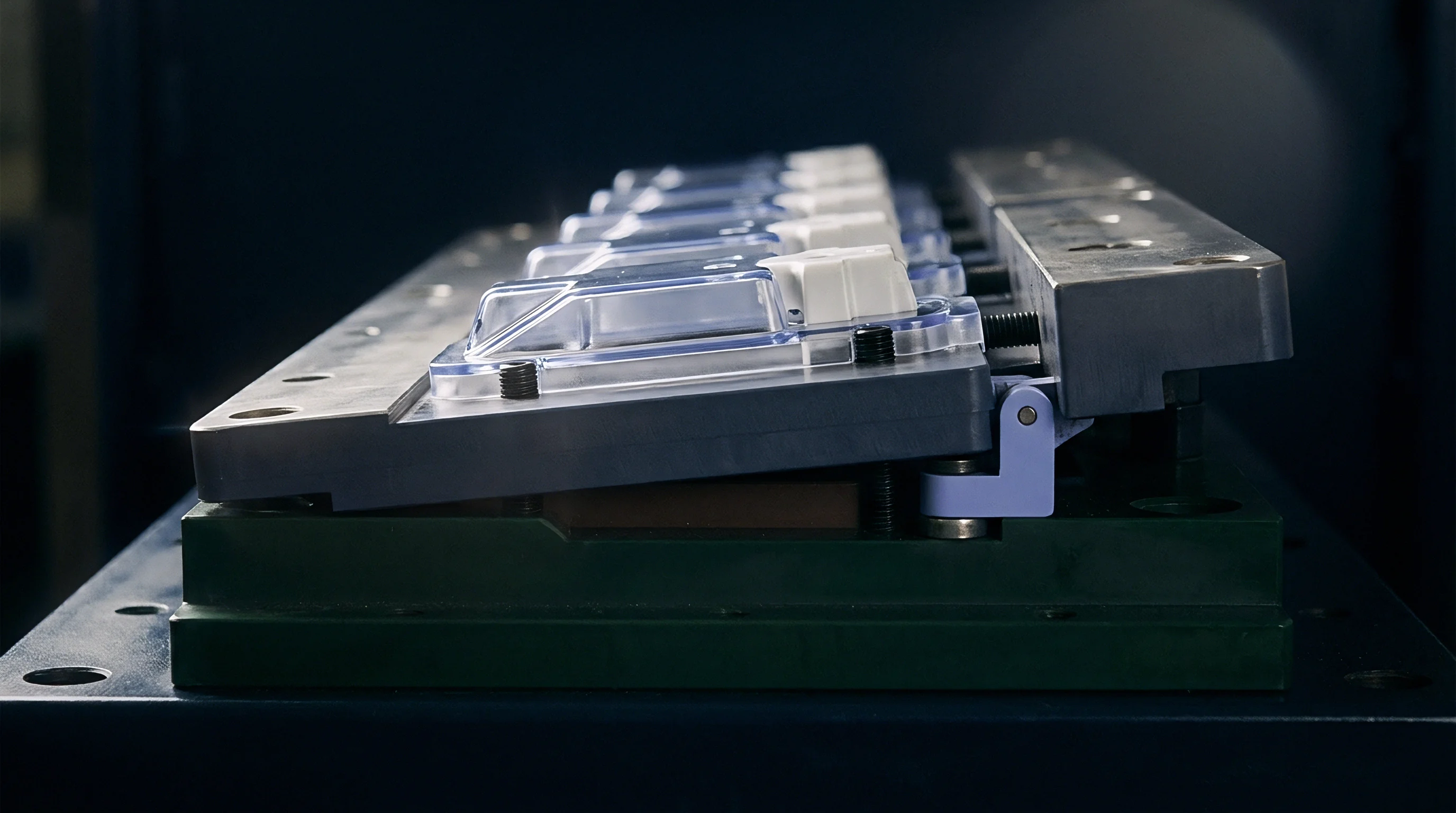 Precision steel mold plates secure translucent polymer housings and white plastic switches across a heavy industrial production workbench.